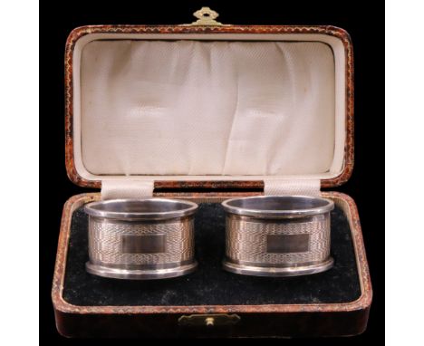 A cased pair of 1930s silver napkin rings, of oval section, each having wavy engine-turned decoration centred by a vacant obl