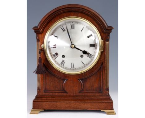 AN EDWARDIAN DOME TOP OAK MANTEL CLOCK with panelled front and ogee bracket feet, silvered convex Roman dial and spring drive