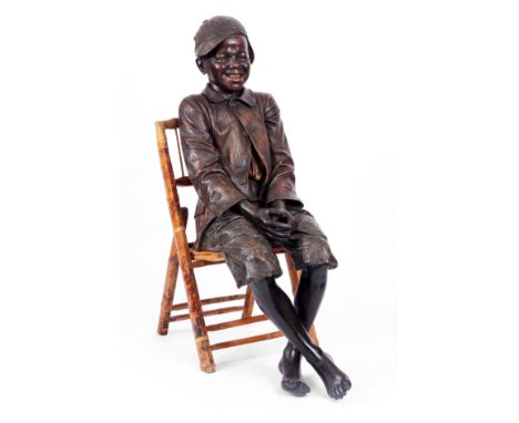 FREDERICK GOLDSCHEIDER, VIENNA A life size Austrian painted terracotta figure of a young boy seated on a bamboo chair in a re