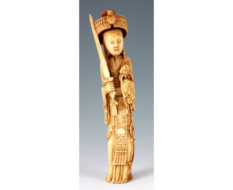 AN ANTIQUE CHINESE IVORY CARVING depicting a diety holding a sword and flower dressed in elaborate robes with sash 24cm high.