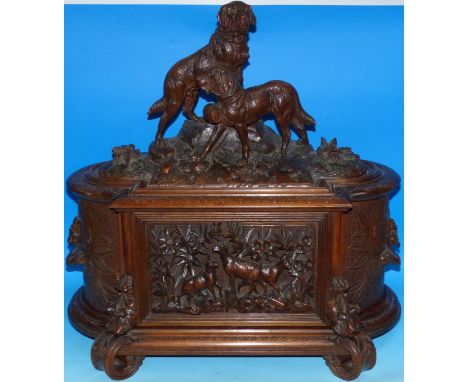 An extensively carved Black Forest Tantalus of rounded rectangular form, the hinged lid and front surmounted by 2 carved St B