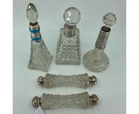 A cut glass scent bottle and stopper with engine turned enamel and silver mount, another with plain silver collar, another th
