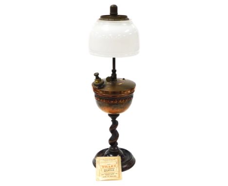 A late 19thC Jacobean Tilley lamp, with a white glass shade, and copper reservoir, embossed with a band of flowers, raised on