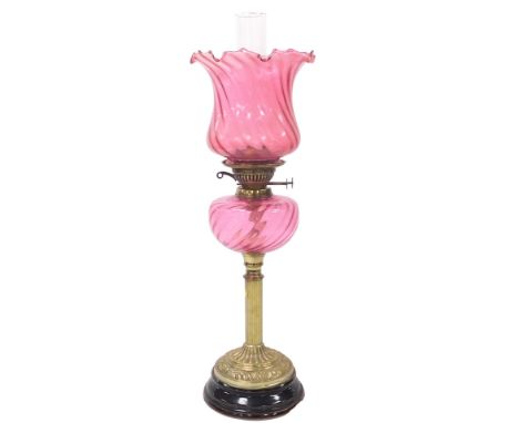 A Victorian brass oil lamp, with a cranberry glass reservoir, glass chimney, and frilled cranberry glass shade, raised on a b