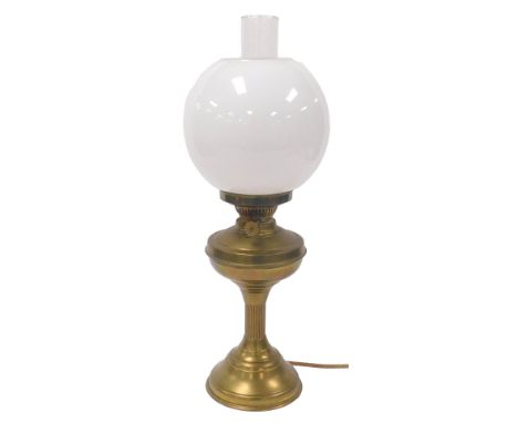 An early 20thC brass oil lamp, converted to electricity, with a glass chimney and white spherical glass shade, 55cm high.Buye