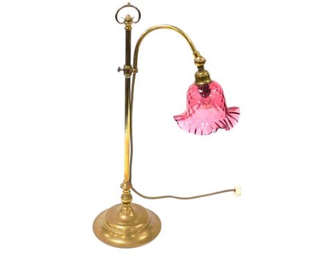 An early 20thC brass oil table lamp, converted to electricity, with a frilled cranberry glass shade, 47cm high. 