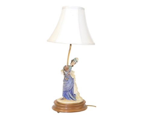 A Capodimonte figural table lamp, designed by P Merli, of a lady standing holding a dog, raised on an oval wooden stand, with