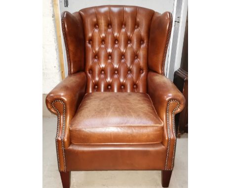A brown leather deep button wing back arm chair with studded edging 