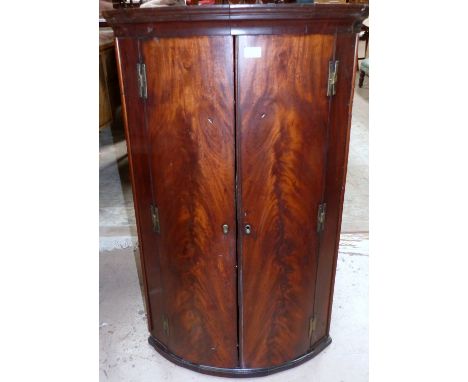 A mid Georgian figured mahogany bow front corner cupboard, fitted 3 shelves and 3 spice drawers