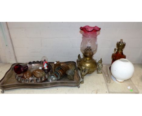 A Victorian brass oil lamp on griffin feet with cranberry shade; another oil lamp; a collection of small copper jelly moulds;
