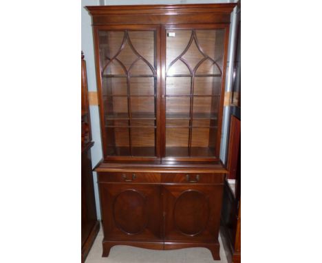 A Georgian style mahogany full height bookcase with twin glazed doors over frieze drawer, and double oval panel cupboard, on 