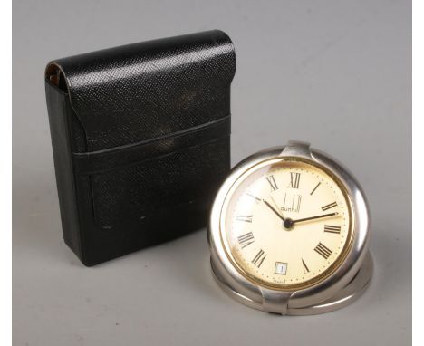 A Dunhill quartz travel alarm clock in case. With Roman numeral markers and date display.  Clock appears to be running. Alarm