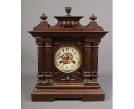 An oak cased mantel clock with brass and enamel dial flanked by twin pillars. Includes key and pendulum.Hx38cm  