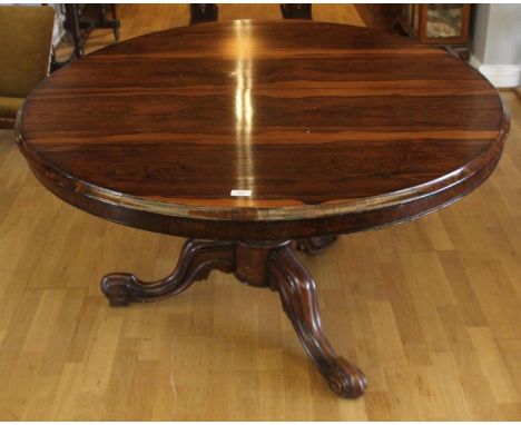 A Victorian rosewood tilt-top dining table raised on a octagonal baluster pedestal with carved tripod legs. 121 cm diameter.