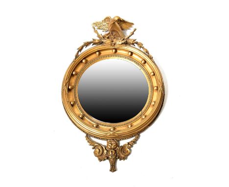 A circular convex gilt wood Empire-style mirror with eagle and wreath finial, the wide circular frame with beaded inner borde