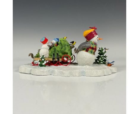 A Holiday tableau figurine of a snowman family. The father is pulling the sleigh with the tree on top, while his children are