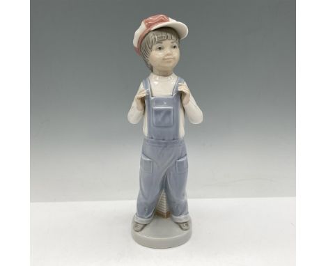Glossy figure of boy wearing a pale red and white hat standing holding his overall straps. An accordion is behind him. Lladro