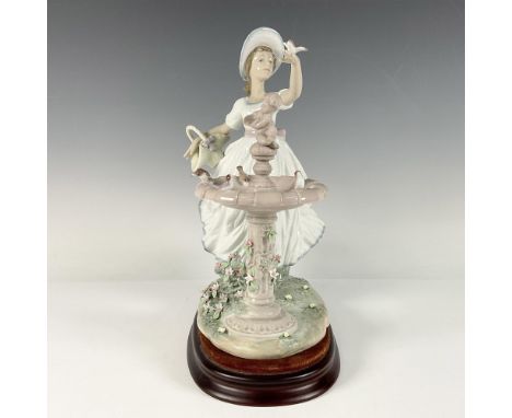 A glossy sculpture portraying a woman in an elegant, flowing white dress, standing beside a bird bath with a bird perched del