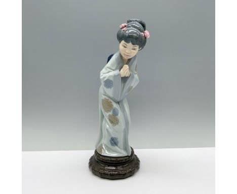 An elegant woman in a blue kimono adorned with flowers, bowing gracefully with her hands clasped. Lladro backstamp. This item