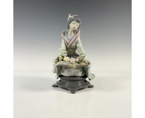 A glossy figure of a woman dressed in a floral kimono, holding a vessel full of delicate flowers. Lladro backstamp. This item