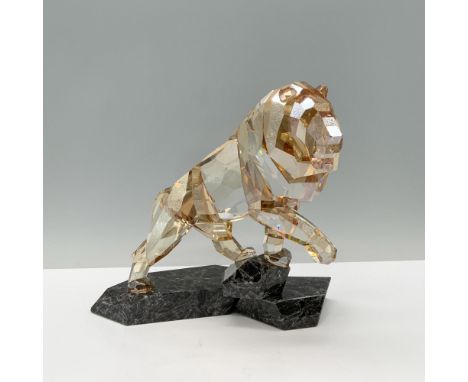 A majestic golden lion, proudly standing with one paw raised on a rugged granite cliff. Swarovski backstamp. This item has it