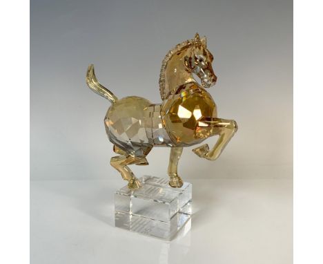 A majestic, amber-colored horse standing confidently, elegantly perched on a clear block engraved with the word horse. Swarov