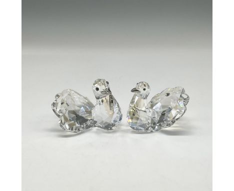 Pair of clear crystal figures with silver-tone beaks. Male holds a metal heart charm in his beak. Female has embedded crystal