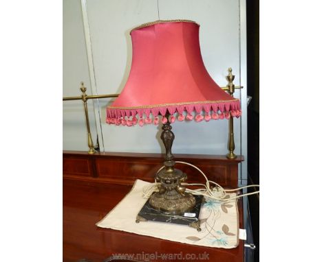 A bronzed effect table Lamp decorated with cherubs and swags, on marble plinth, with red shade, 26" tall.