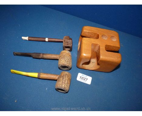 Three vintage rustic wooden pipes, one with carved face and a three bay pipe holder.