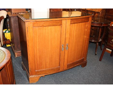 A bow front mahogany cabinet, twin panel doors with brass oval drop handles enclosing a drawer and three adjustable shelves, 