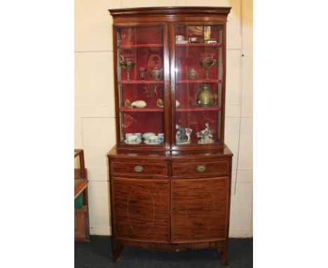 An Edwardian inlaid mahogany bow front display cabinet, top with twin glazed doors and sides enclosing three shelves, on base