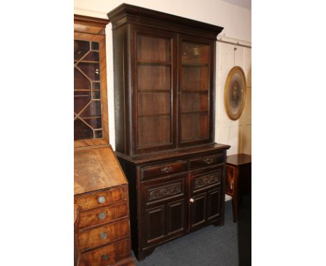 A late 19th/early 20th century oak bookcase, with twin glazed panel doors enclosing three shelves, above two drawers and cupb