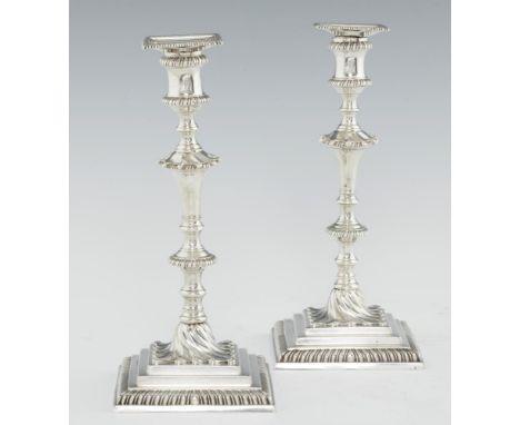 A PAIR OF GEORGE III GADROONED SILVER CANDLESTICKS with waisted sconce, swirl base and stepped square foot, crested, nozzles,