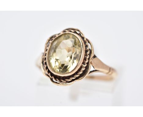 A 9CT GOLD CITRINE RING, designed with a central oval cut citrine within a collet mount, rope twist and scallop edge surround