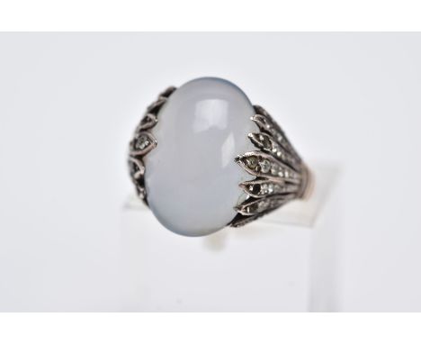 A YELLOW METAL GEM SET RING, designed with a milky chalcedony cabochon, openwork feathered shoulders set with colourless past