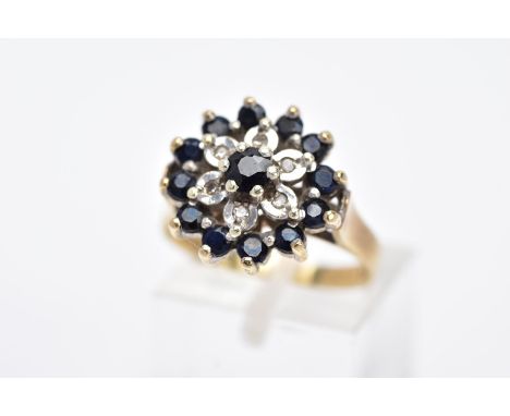 A 9CT GOLD SAPPHIRE AND DIAMOND CLUSTER RING, the raised cluster set with a claw set, circular cut blue sapphire, with a surr