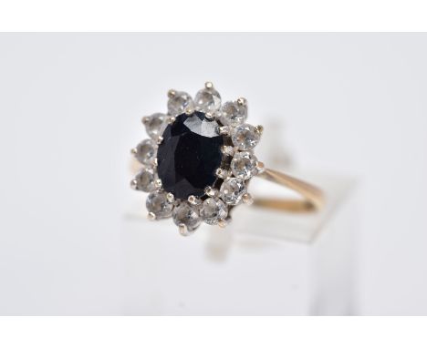 A 9CT GOLD CLUSTER RING, designed with a central oval cut blue sapphire, within a surround of claw set, colourless, circular 