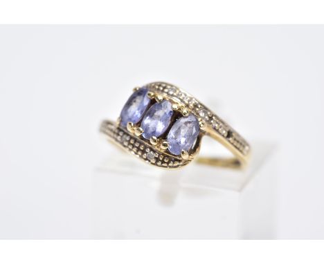 A YELLOW METAL GEM SET RING, of a crossover design, set with three oval cut purple stones assessed as iolite, within single c