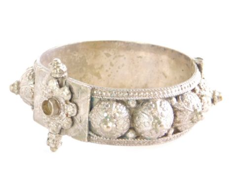 A Middle Eastern white metal hinged bangle, decorated overall with roundels etc.