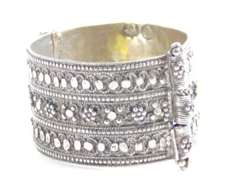 An Indian bangle, raised with three banks of flower heads with an elaborate clasp, unmarked, 5cm wide. 