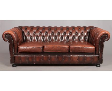 A brown leather deep buttoned Chesterfield three seater sofa.  Small tear to back left corner side. Cracking to material towa