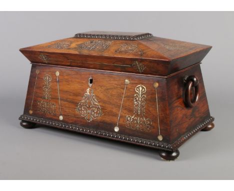 A Victorian rosewood tea caddy of sarcophagus form, having mother of pearl inlay and wooden loop handles.  Part of escutcheon