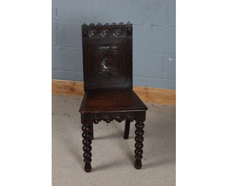 A 19th century carved oak hall chair, with a wavy cresting rail above three circular lozenges and a tapering seat above bobbi