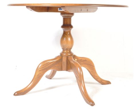 A vintage late 20th century Ercol beech and elm wood circular extending dining table being raised on a tripod base with exten