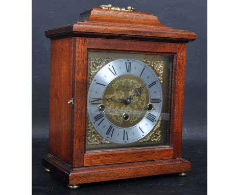 A contemporary Woodford oak cased mantel clock having a brass handle with a pediment top, a silvered and brass clockface havi