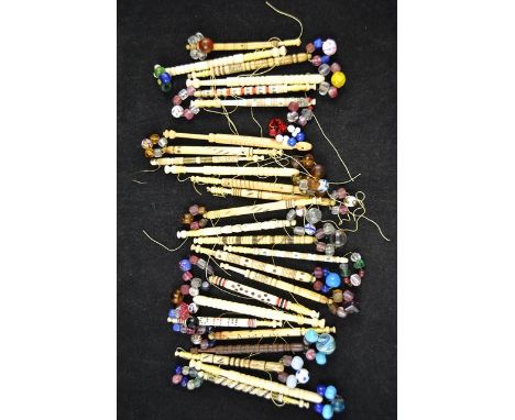 Twenty-five bone vintage lace bobbins with coloured beads, together with a wooden lace bobbin