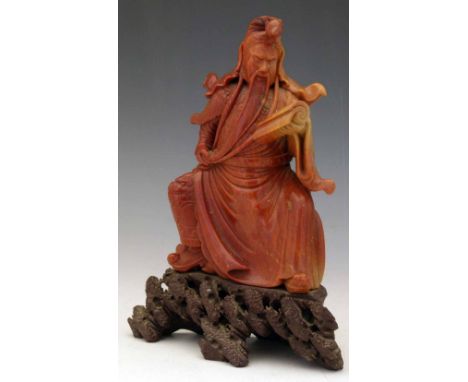 Chinese red soapstone figure of the seated Guandi on a rocky outcrop, reading a scroll, height 24cm.    Condition report:  a 