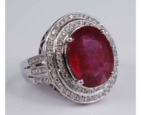 A contemporary 14ct white gold, ruby and diamond cluster ring, arranged as central four-claw set oval cut ruby measuring appr