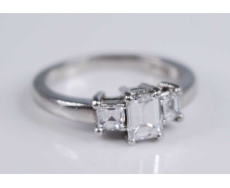 A platinum diamond three stone ring, featuring a centre emerald cut with an asscher cut diamond on either side, all in claw s