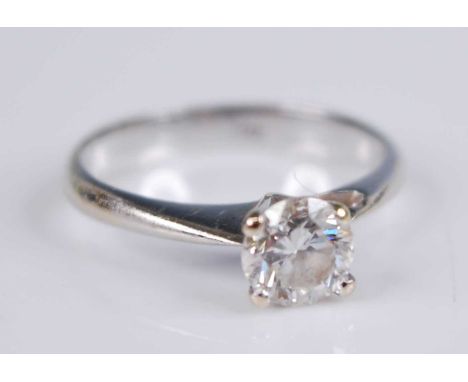 A white metal diamond solitaire ring, with a round brilliant cut diamond in a four-claw V shaped setting with a single heart 